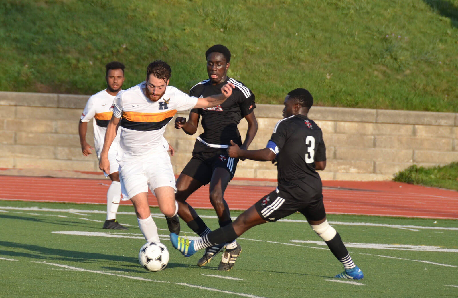 Two opponent players trying to steal the soccer ball from two Humber players