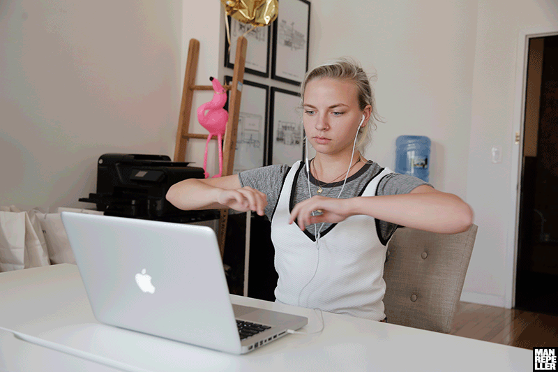 Girl wearing earphones stretches in her chair in front of her Mac laptop