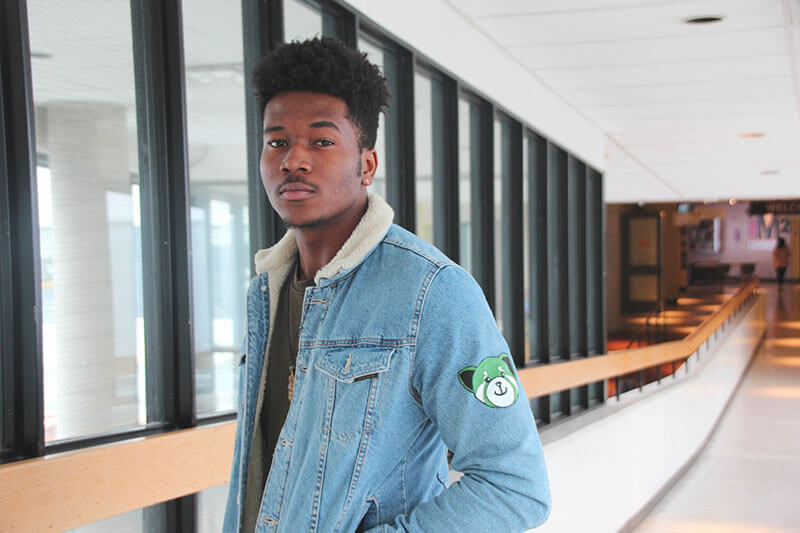 Student standing in long hallway wearing custom jacket.