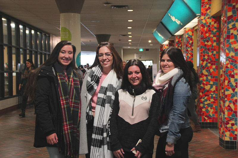 Four students posing with each other wearing scarves in long hallway.