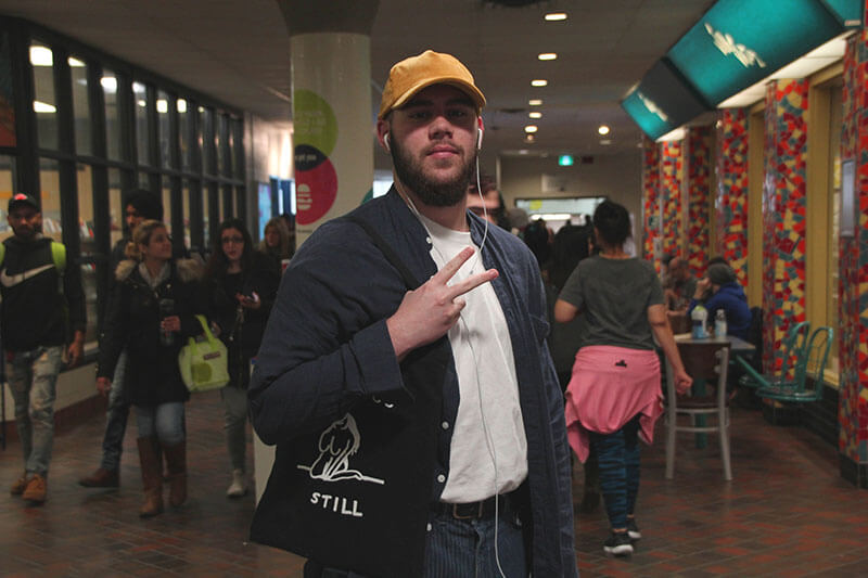 Student wearing hat poses in hallway full of people.