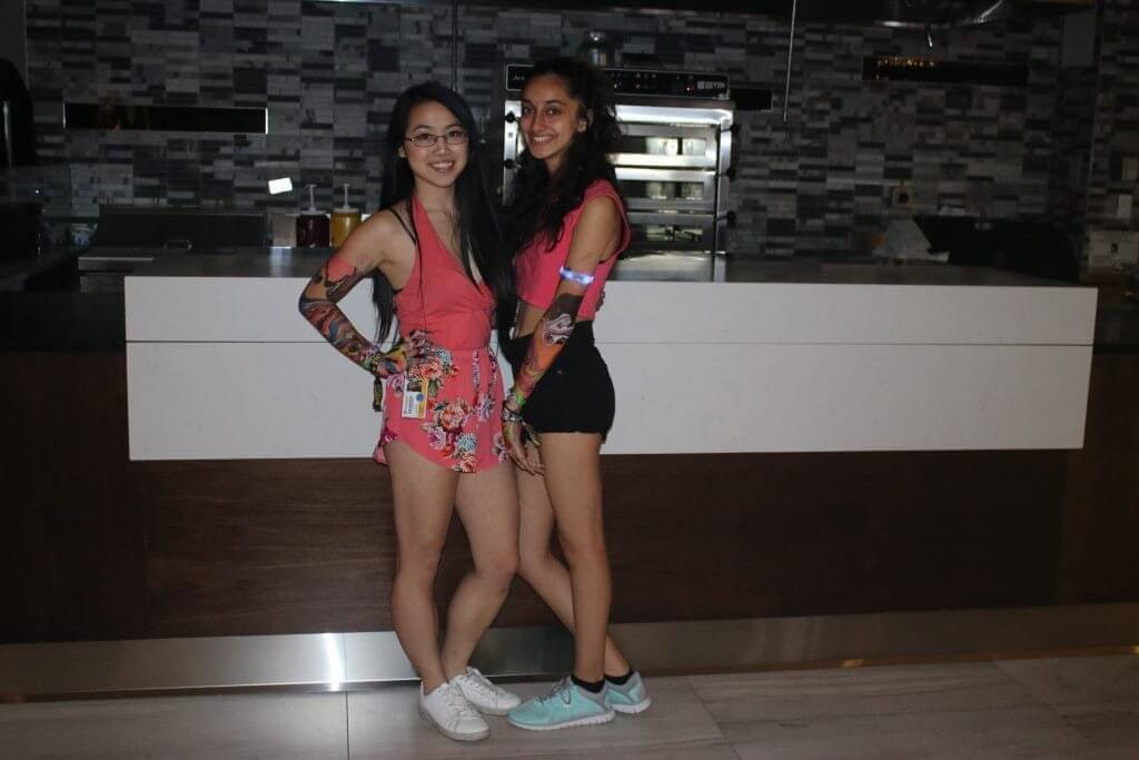 Two girls one with multicoloured shorts and pink top and another with black shorts and pink top