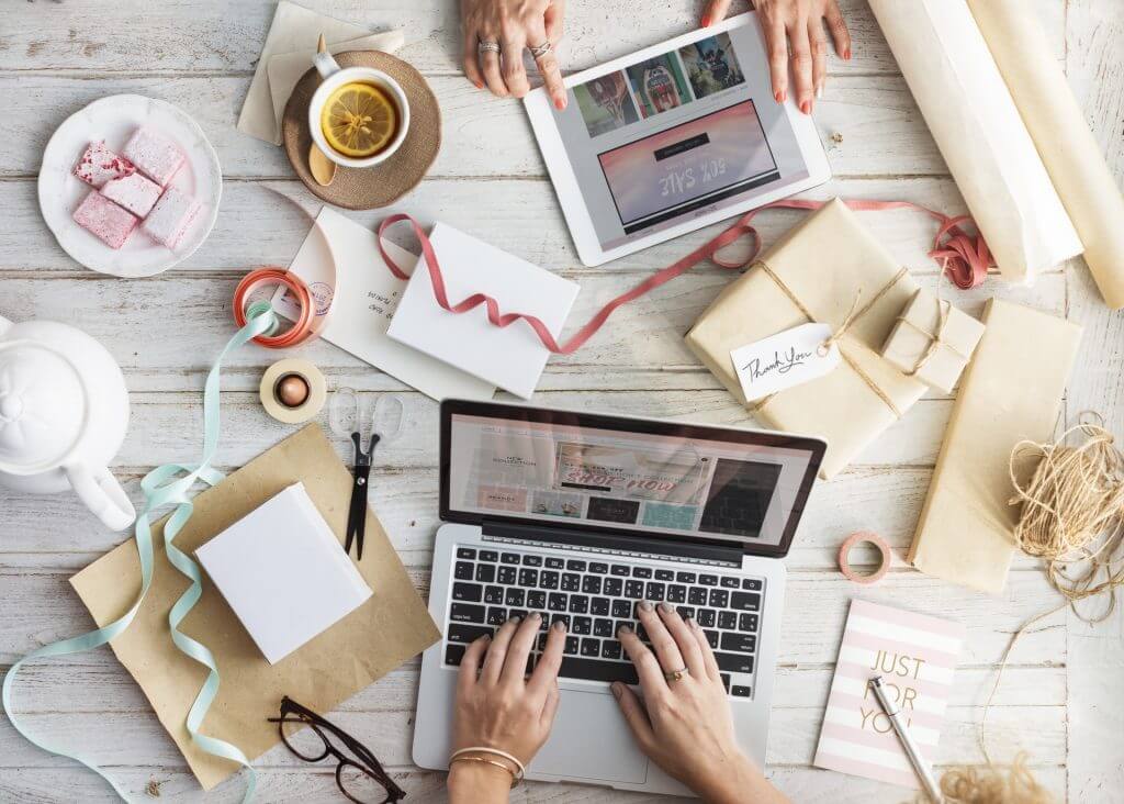 A bird's-eye-view of a tablet, laptop, and gift supplies on a desk