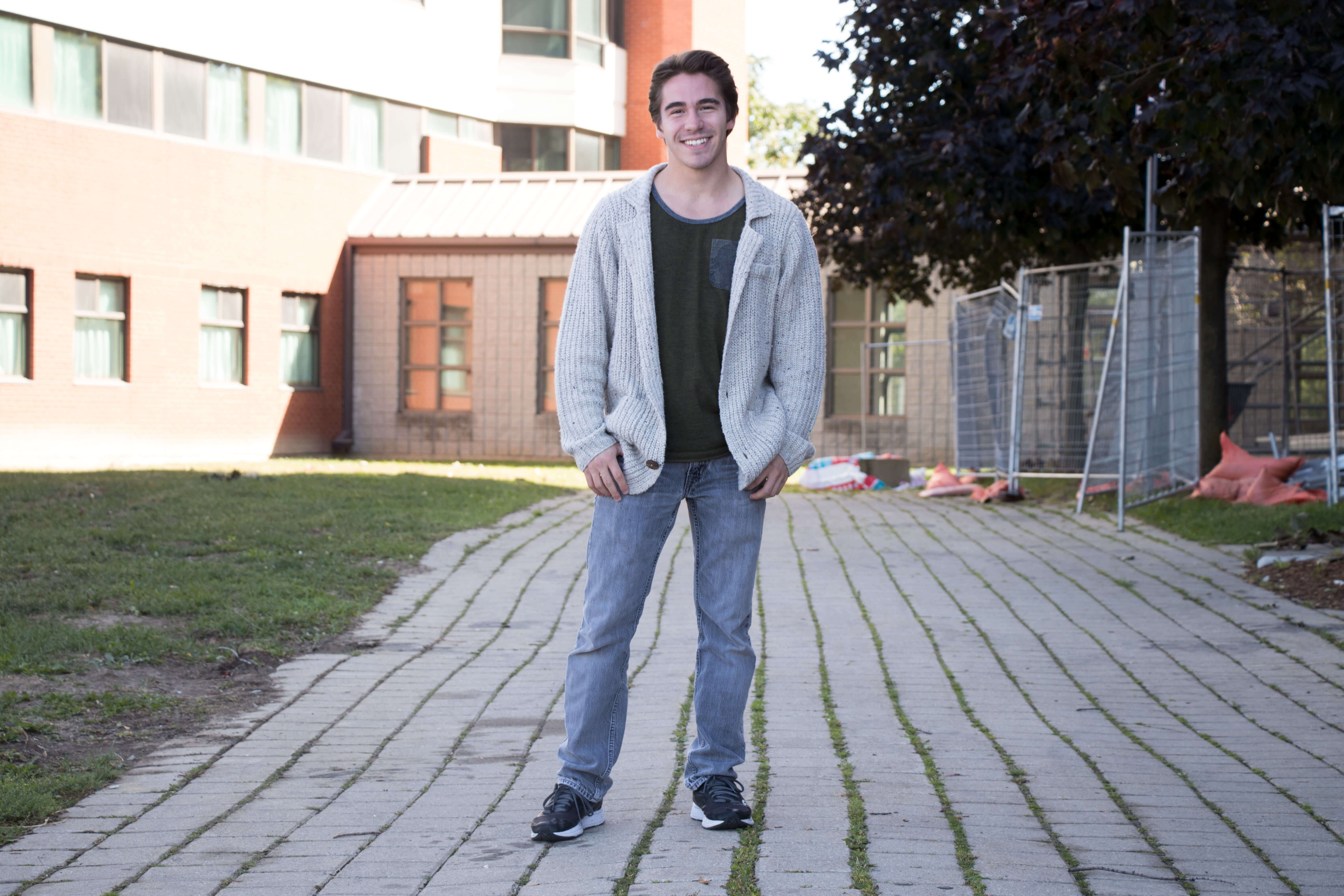 Guy standing and smiling wearing a cardigan, jeans and running shoes