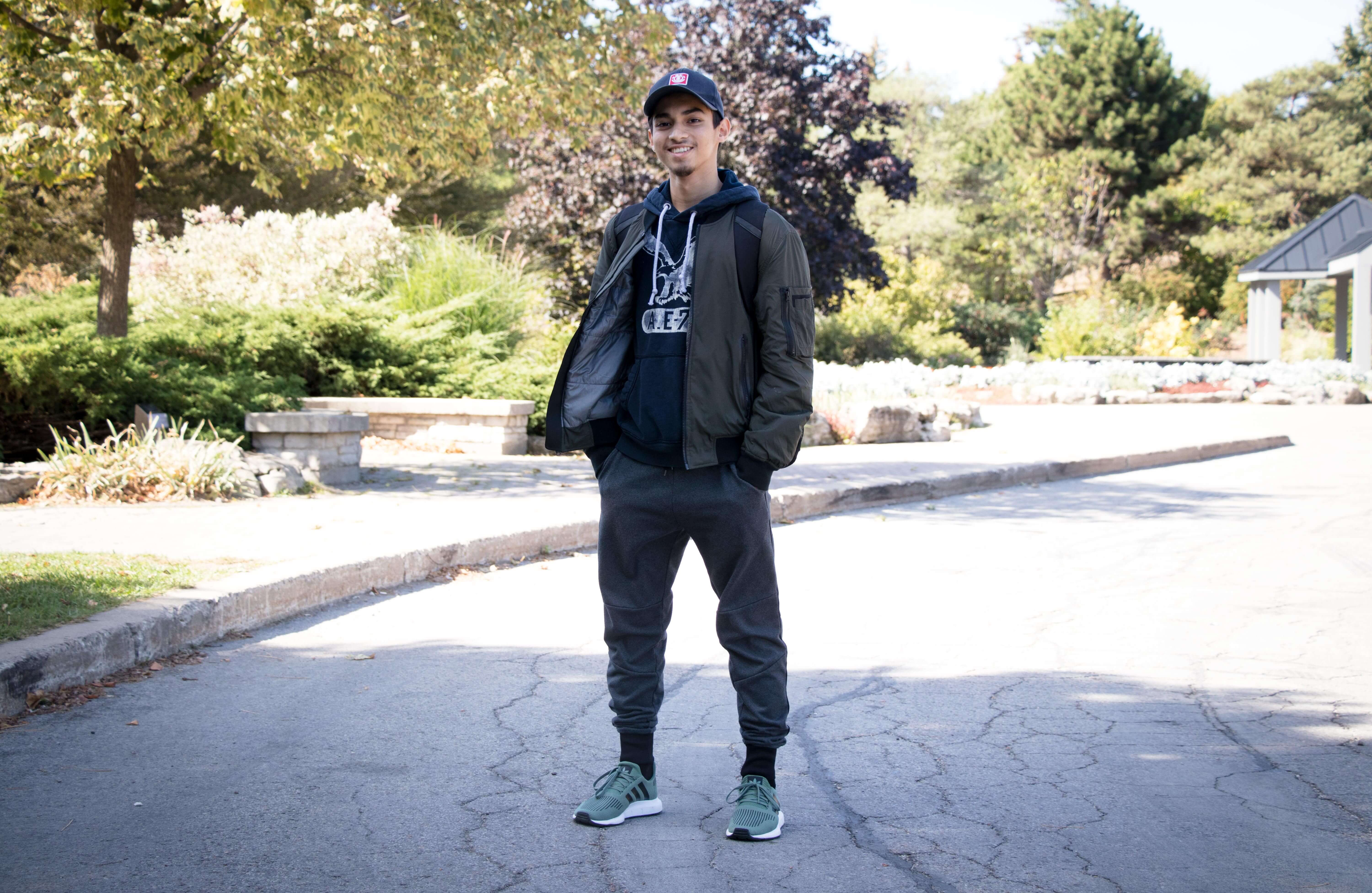 Guy standing outdoors and smiling wearing jacket, sweatpants and running shoes 