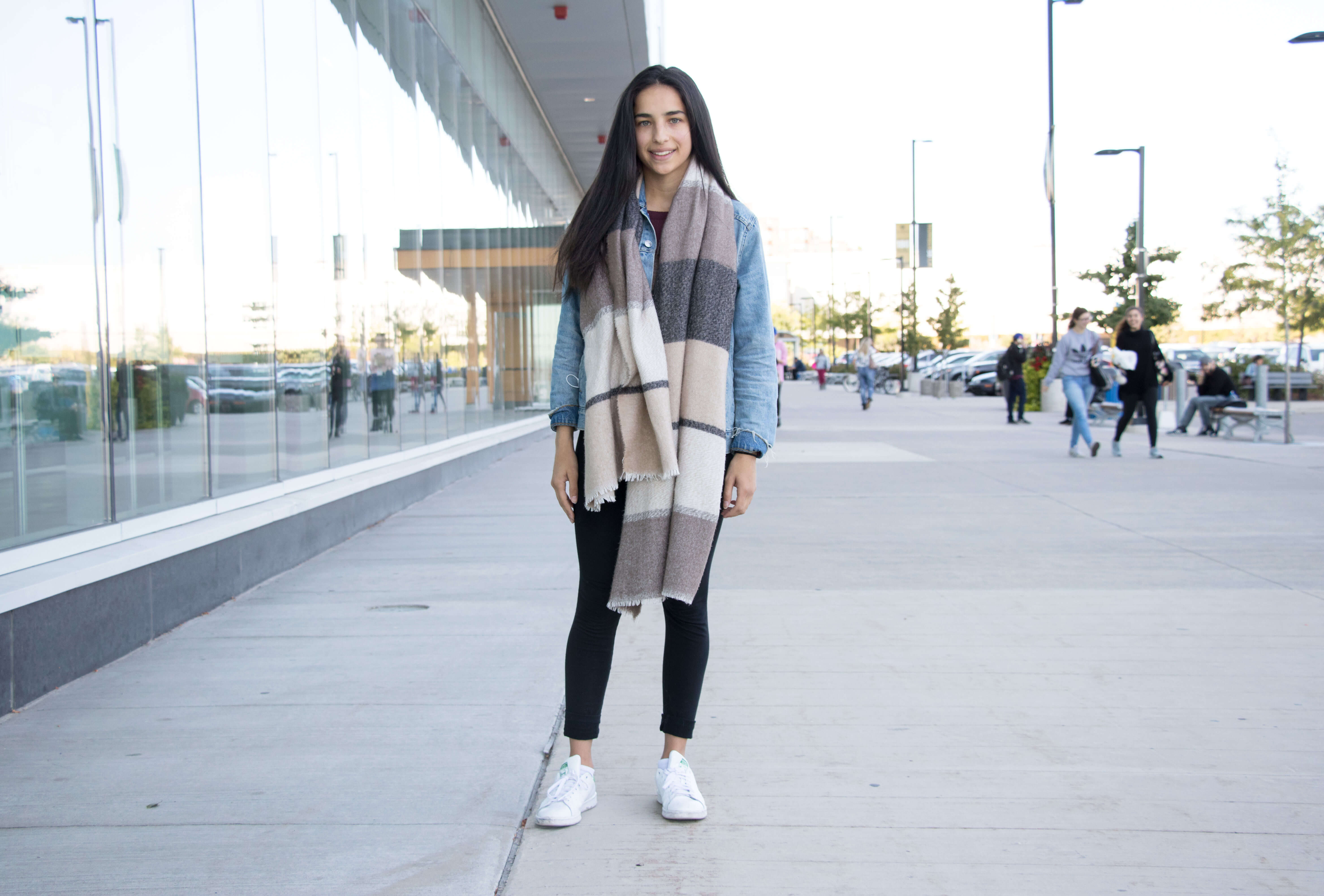 Girl standing and smiling wearing a scarf and denim jacket and sneakers