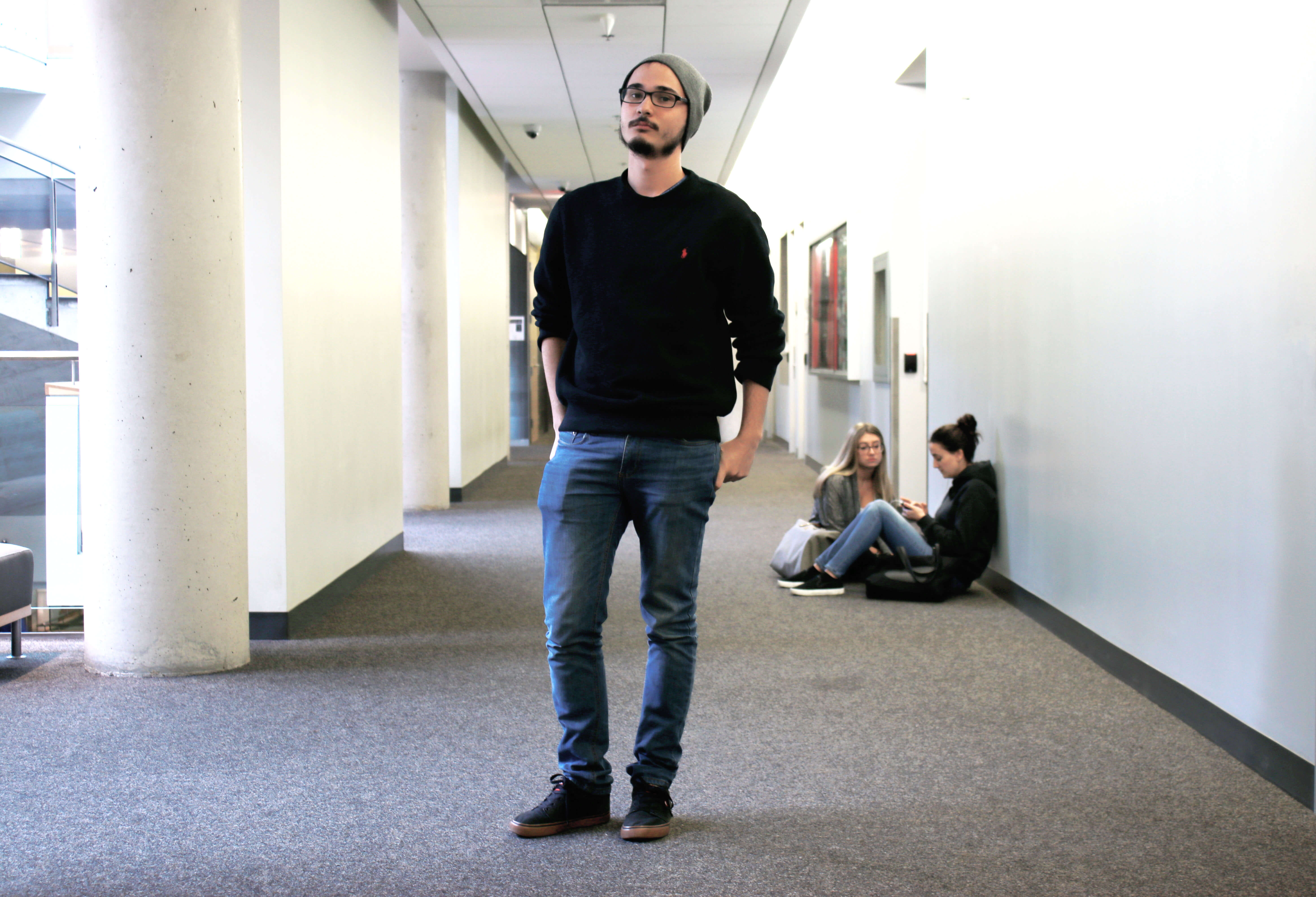Guy standing in hallway wearing a sweater and jeans