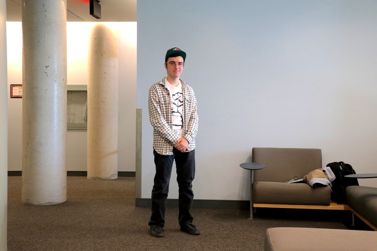 Man wearing baseball hat, flannel, and black jeans.