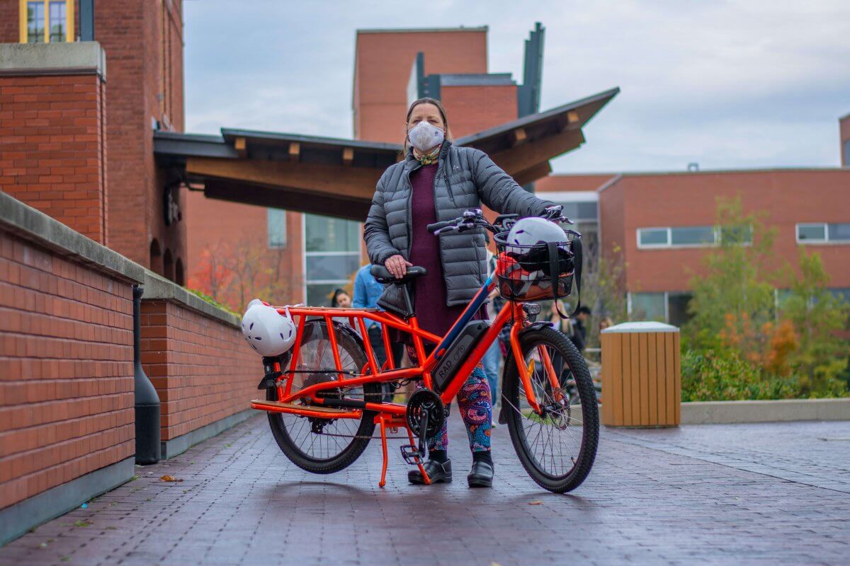woman wearing a mask, standing behind a large bicycle