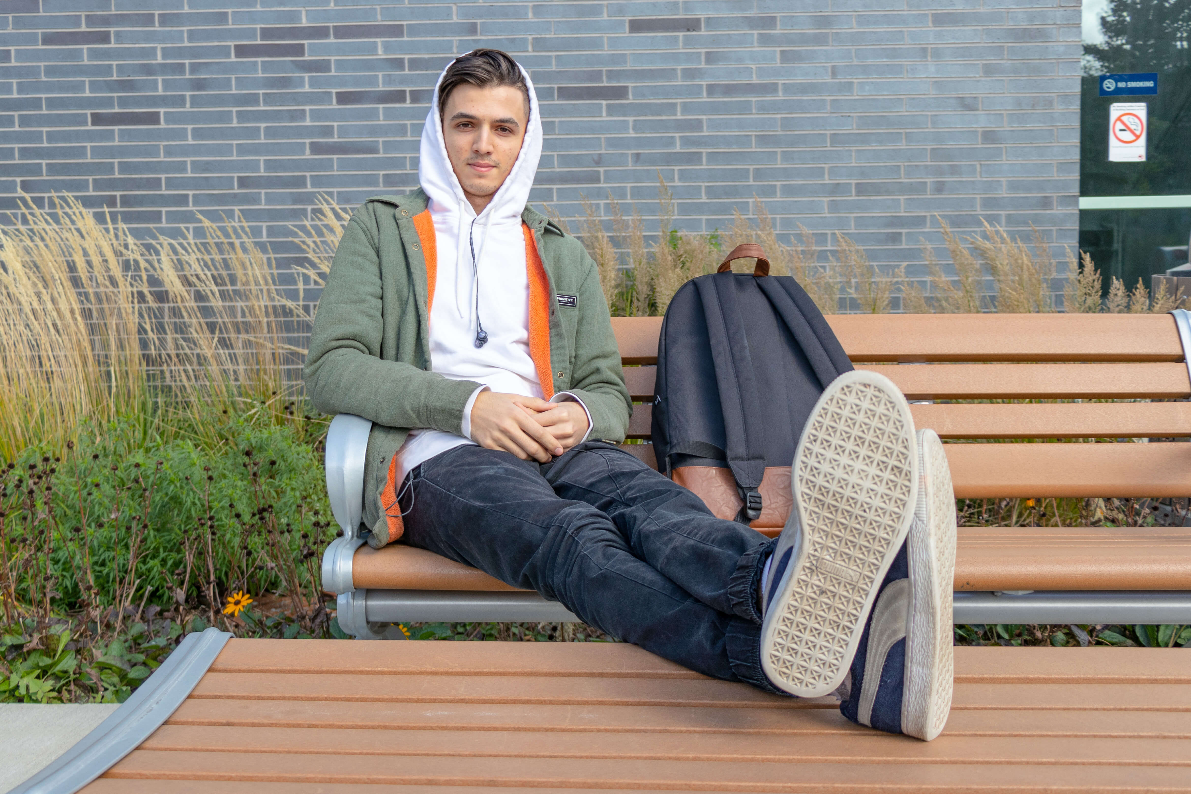 Male student with feet up on bench looks at camera