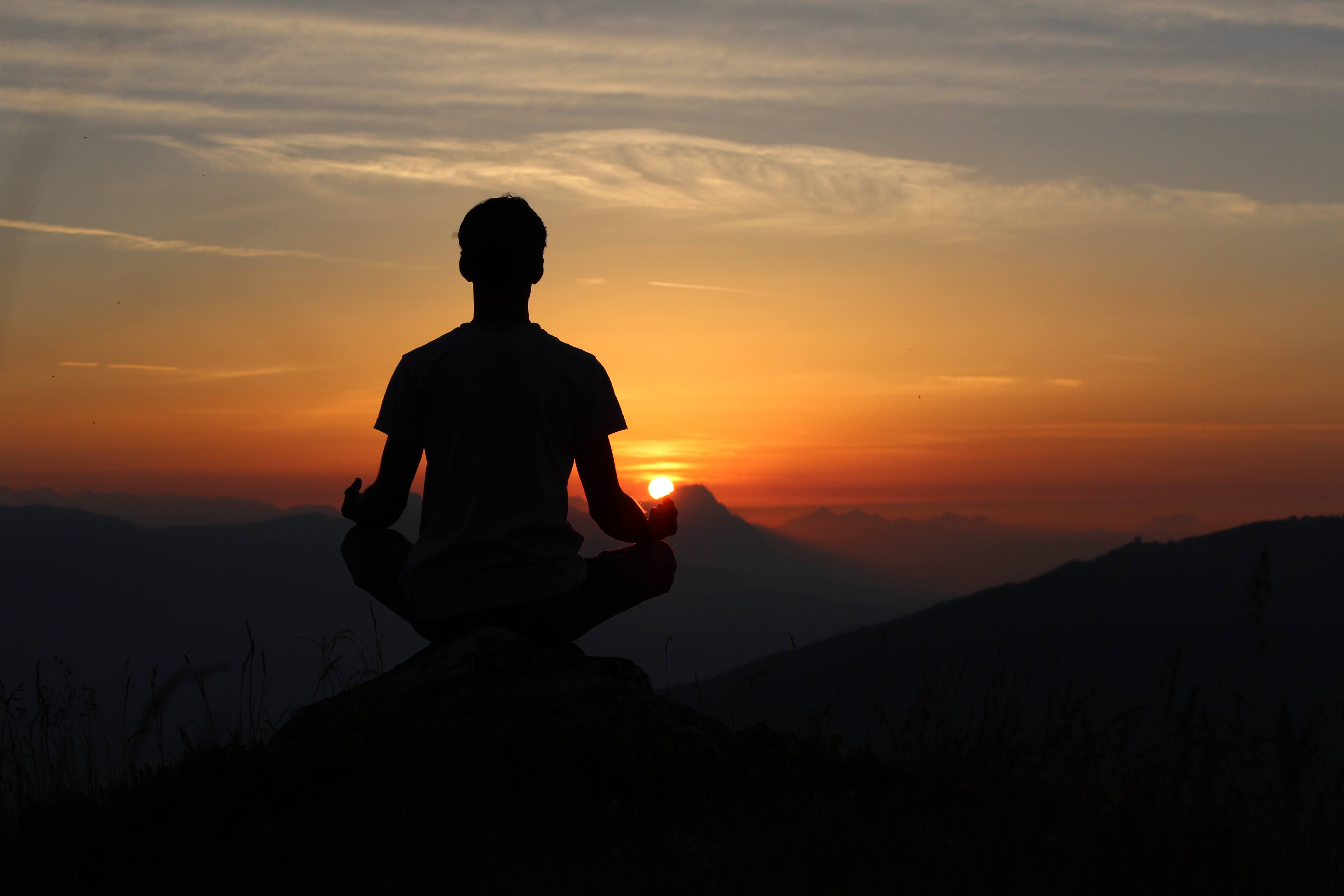 man sits on hill at sunset