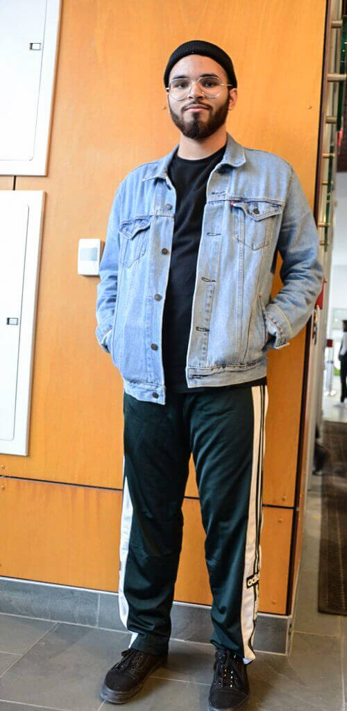 student in denim poses against wall