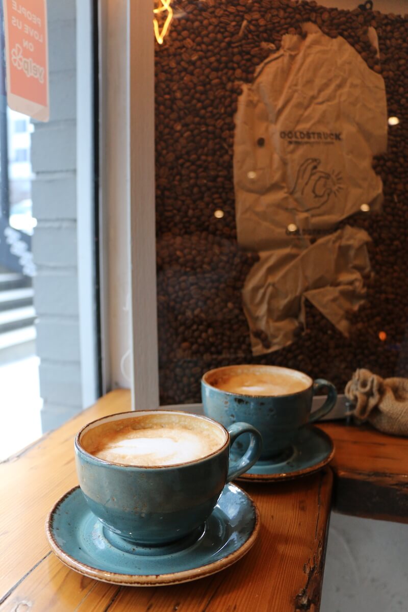 2 cappuccinos on table with coffee beans behind them