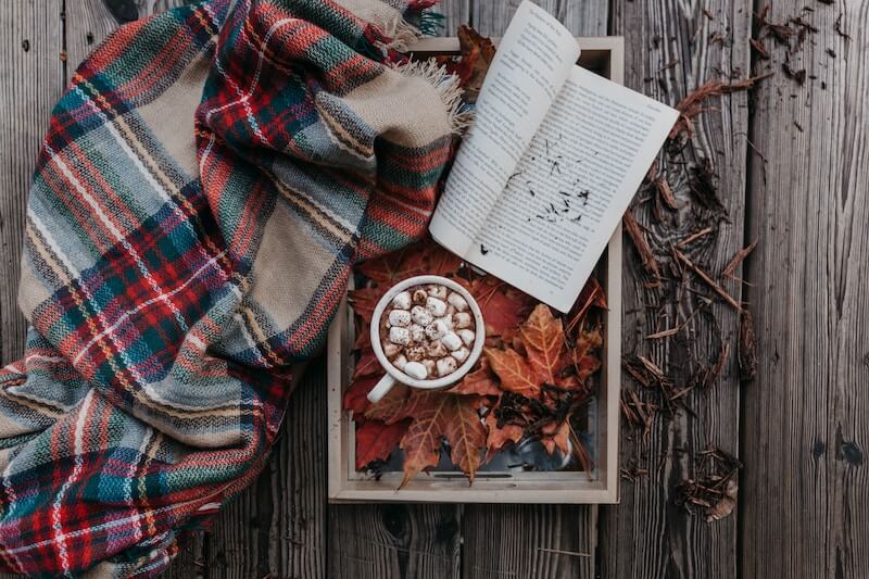 Blanket next to hot chocolate and book