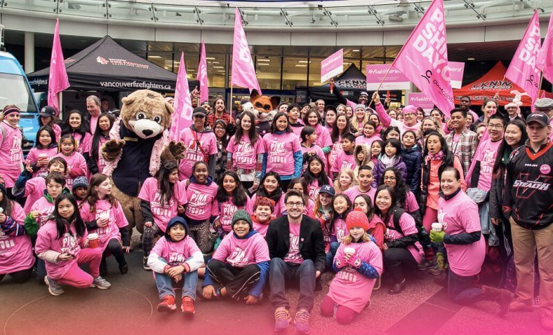 Crowd of people holding pink flags and wearing pink shirts for Pink Shirt Day