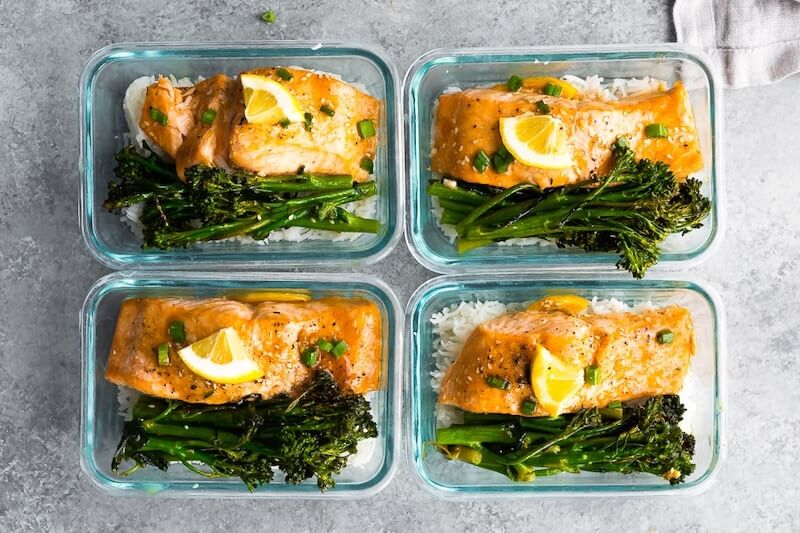 4 glass containers with salmon lemon wedge on top and side of brocollini