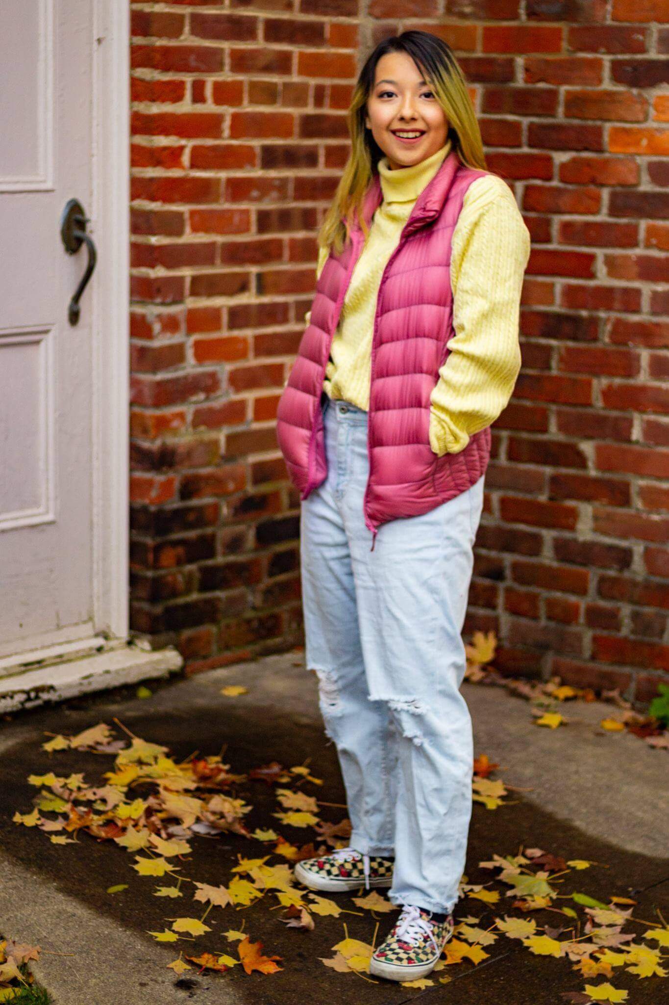 girl standing in front of house door which hands in vest pockets.