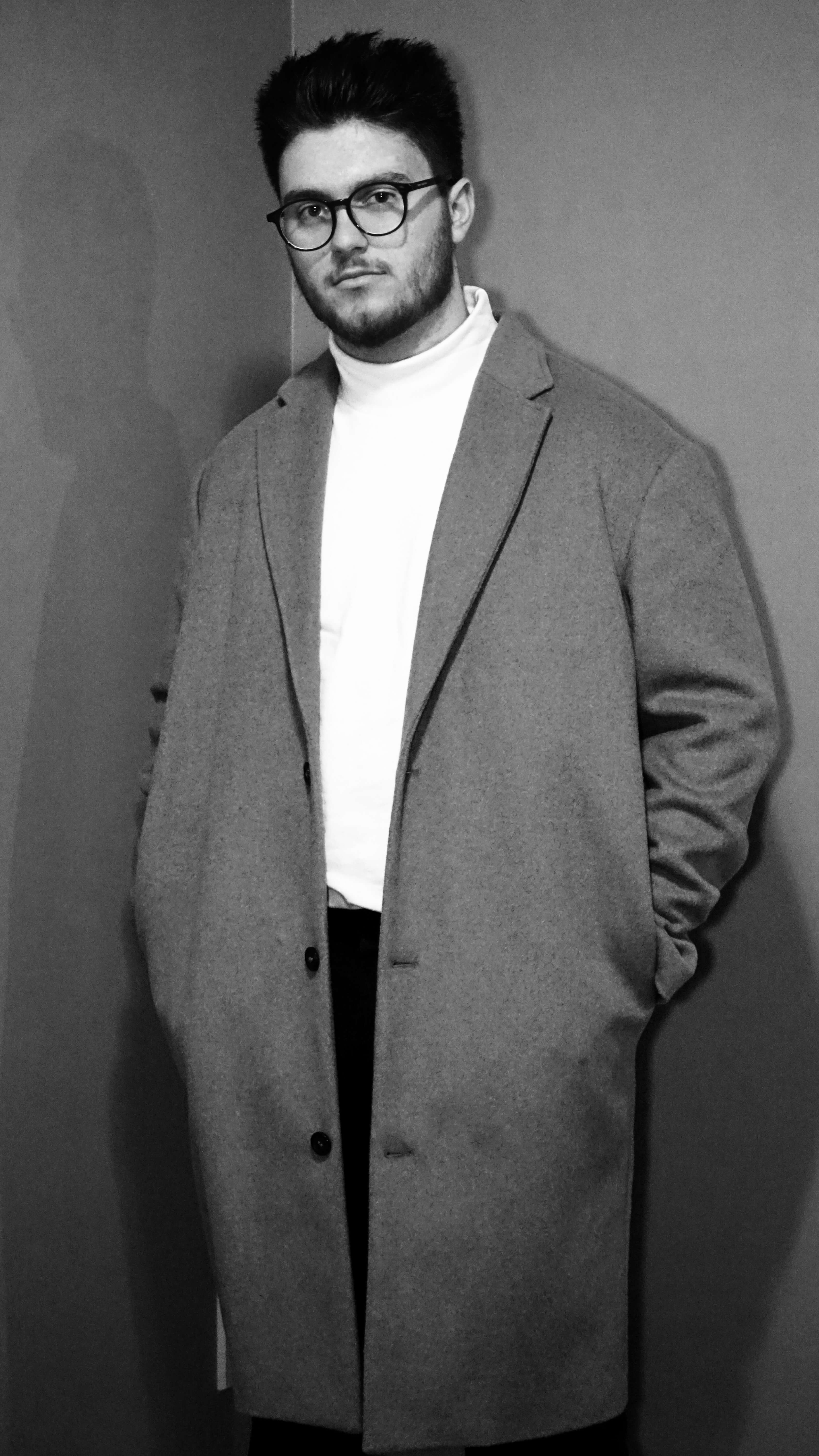 Man standing with hands in pocket in long jacket.