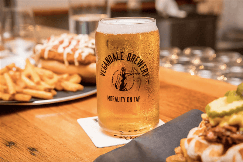 Cup of beer in cup reading "Vegandale Brewery / Morality on tap" with french fries and sandwiches in background
