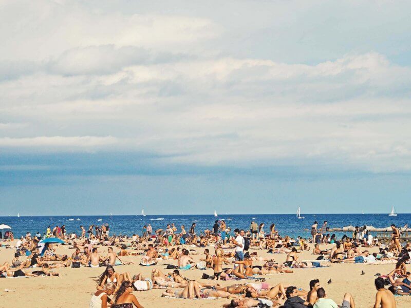 Beach filled with crowd of people sunbathing