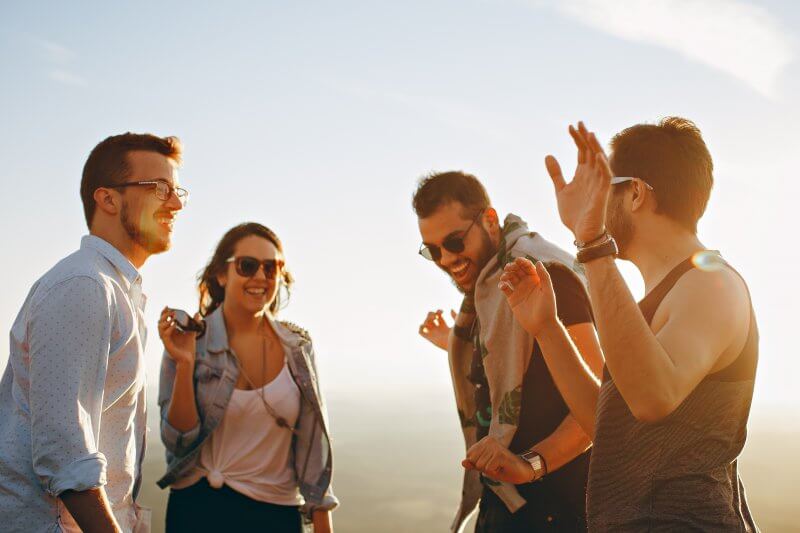 Group of 3 men and 1 women wearing glasses and laughing in front of sky scenery