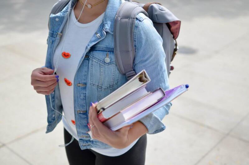 body shot of person wearing backpack and carrying books