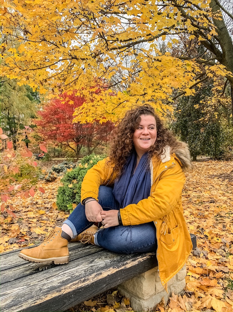 girl sitting on bench in front of colourful trees