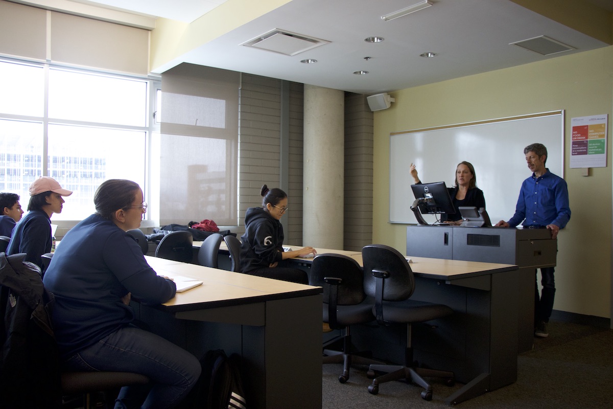 man and woman speaking to a class of students