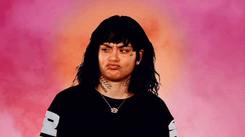 Singer Kehlani purses her lips and looks skeptically to the side on a pink and orange backdrop.