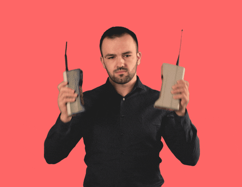 A man in a black shirt holds two old-fashioned cell phones up to his ears.