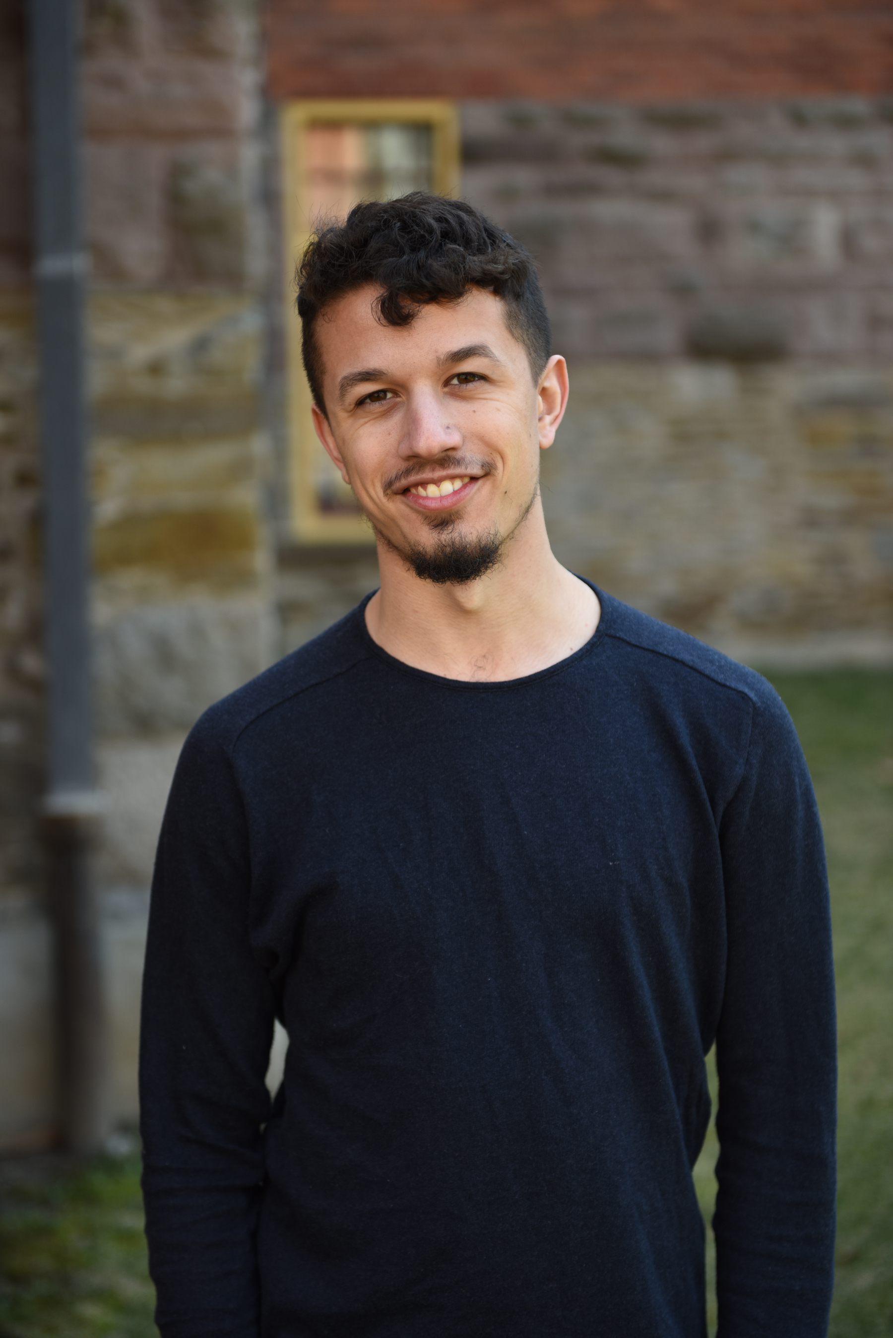 Fourth year Humber College Bachelor of International Development student Graham Budgeon stands outdoors wearing a navy blue shirt and smiles.