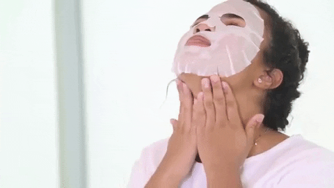 A young woman wears a sheet face mask and dances contently.