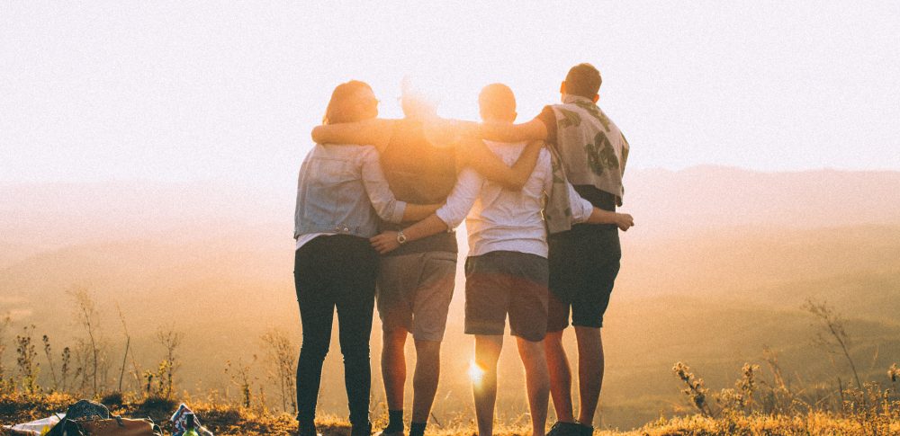 Four people standing in a line with their arms draped around each other