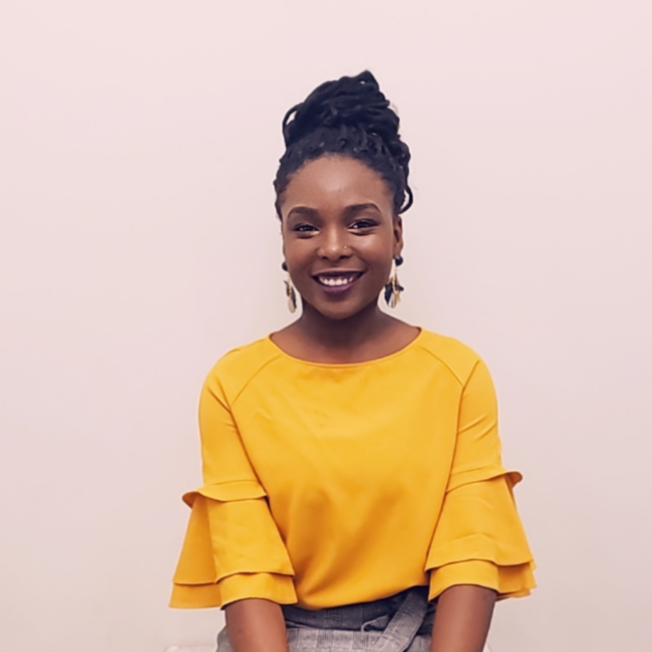 Keithtian Green, IGNITE 2020-2021 Board of Directors member at Humber College North campus wears a yellow long sleeved shirt, feather earrings and a braided updo. She smiles at the camera.
