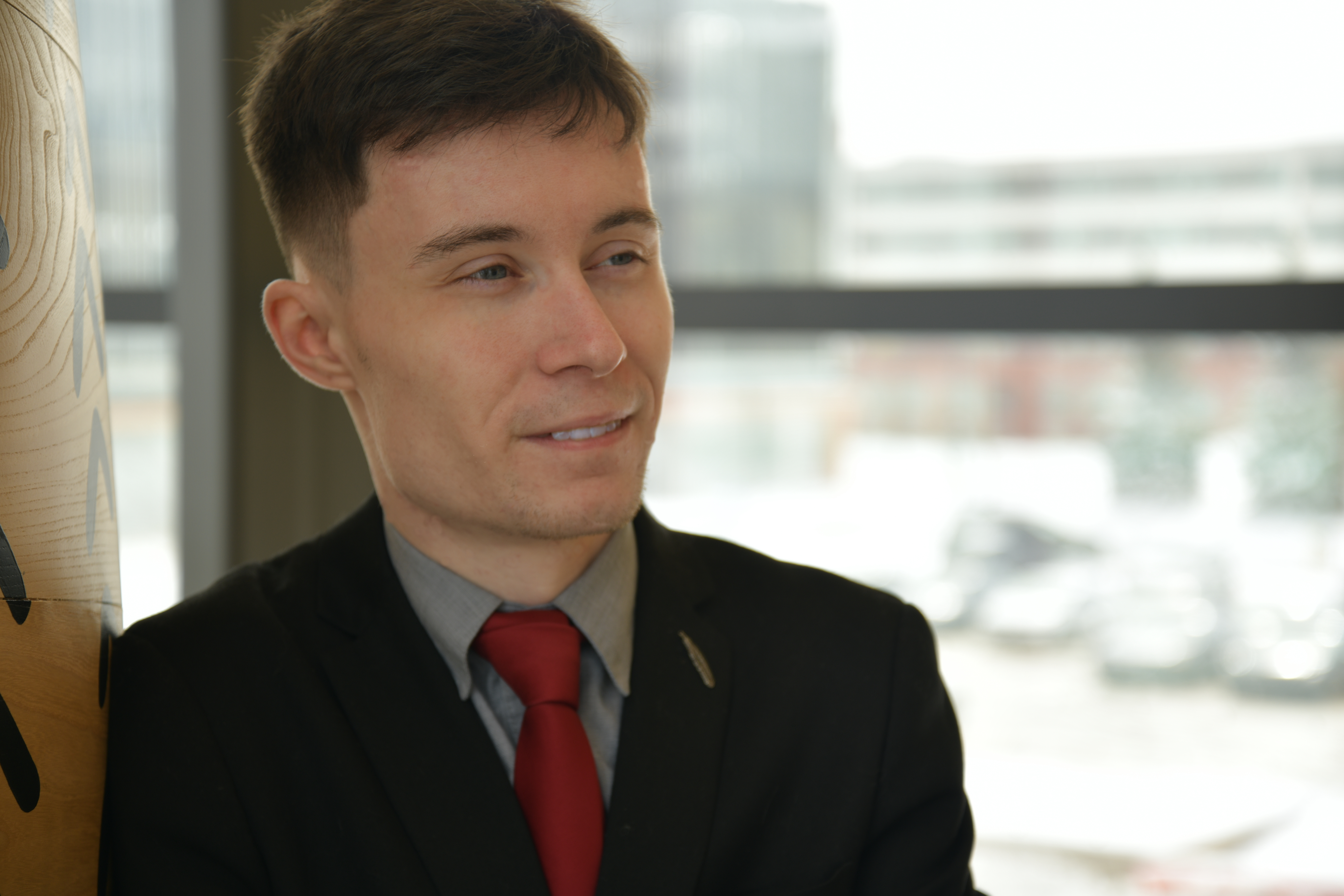 IGNITE 2020-2021 Board of Directors chair Eli Ridder wears a black suit with a grey dress shirt and a red tie while looking off into the distance.