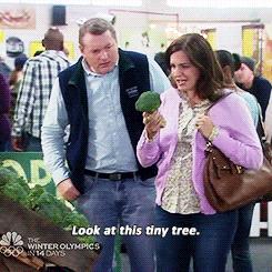 Scene from "Parks and Recreation" where a female citizen in a purple cardigan with brown hair holds up a piece of broccoli and says, "Look at this tiny tree!"