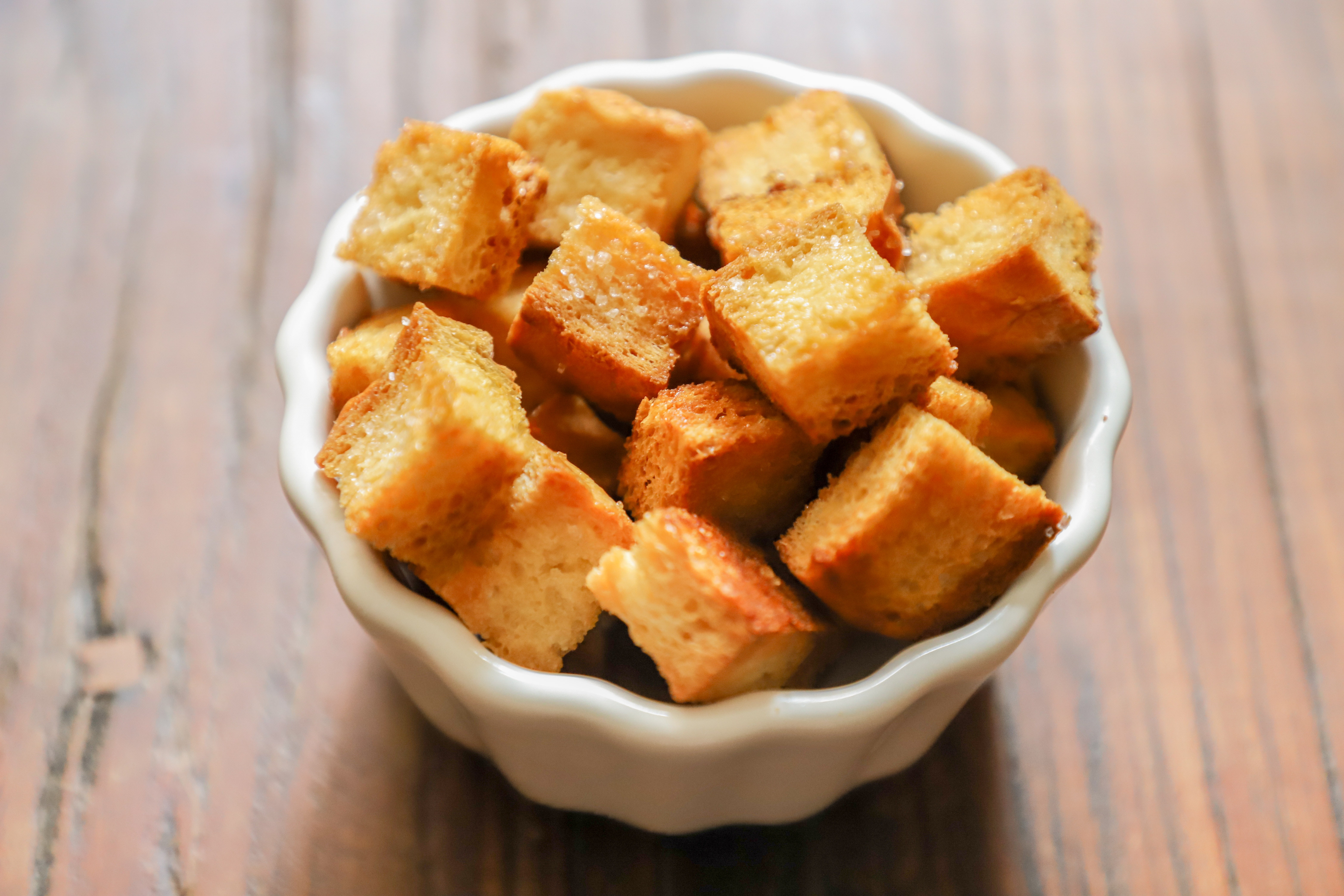A white veramic bowl is filled with golden brown croutons.