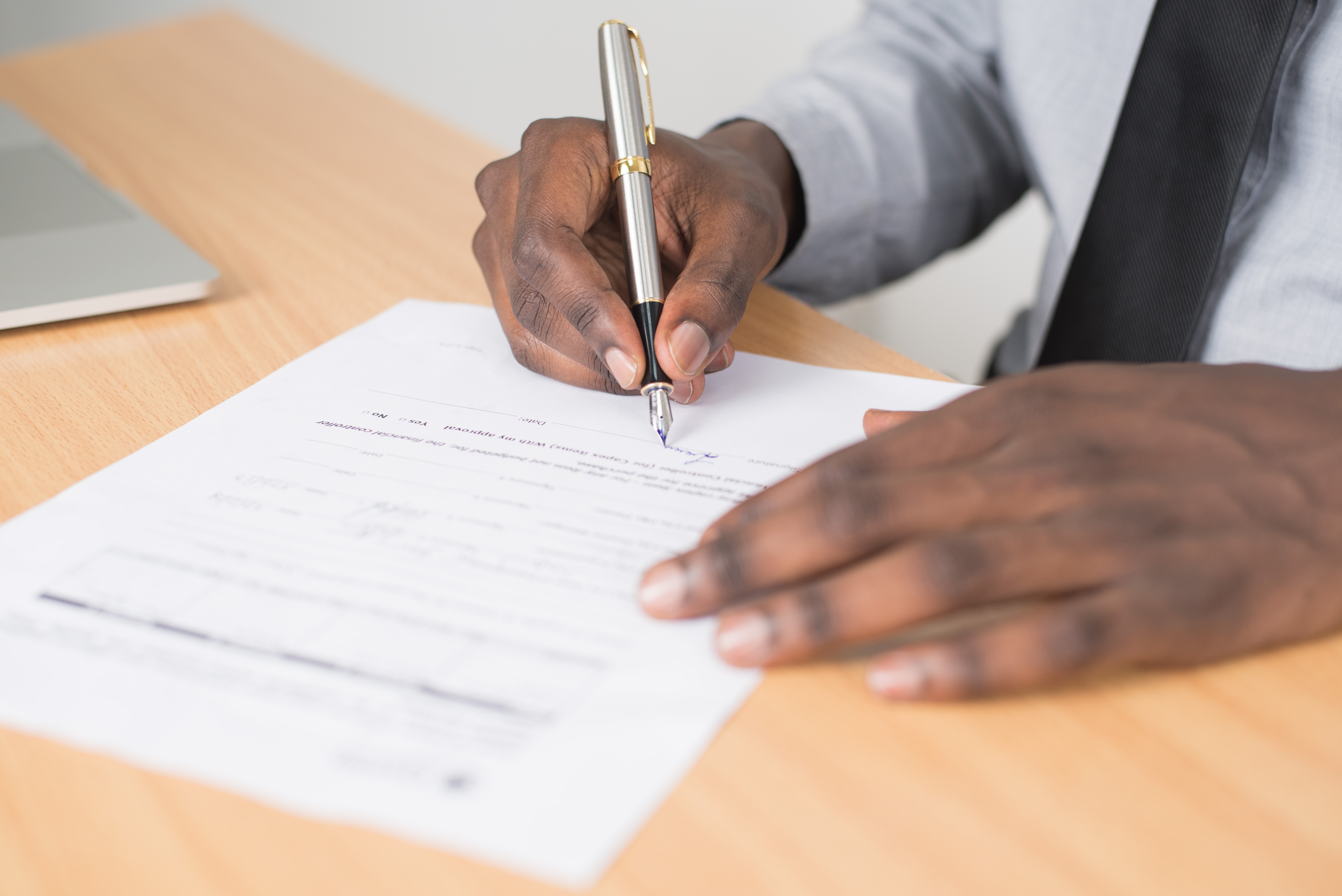 A person fills out a form on white paper with a pen.