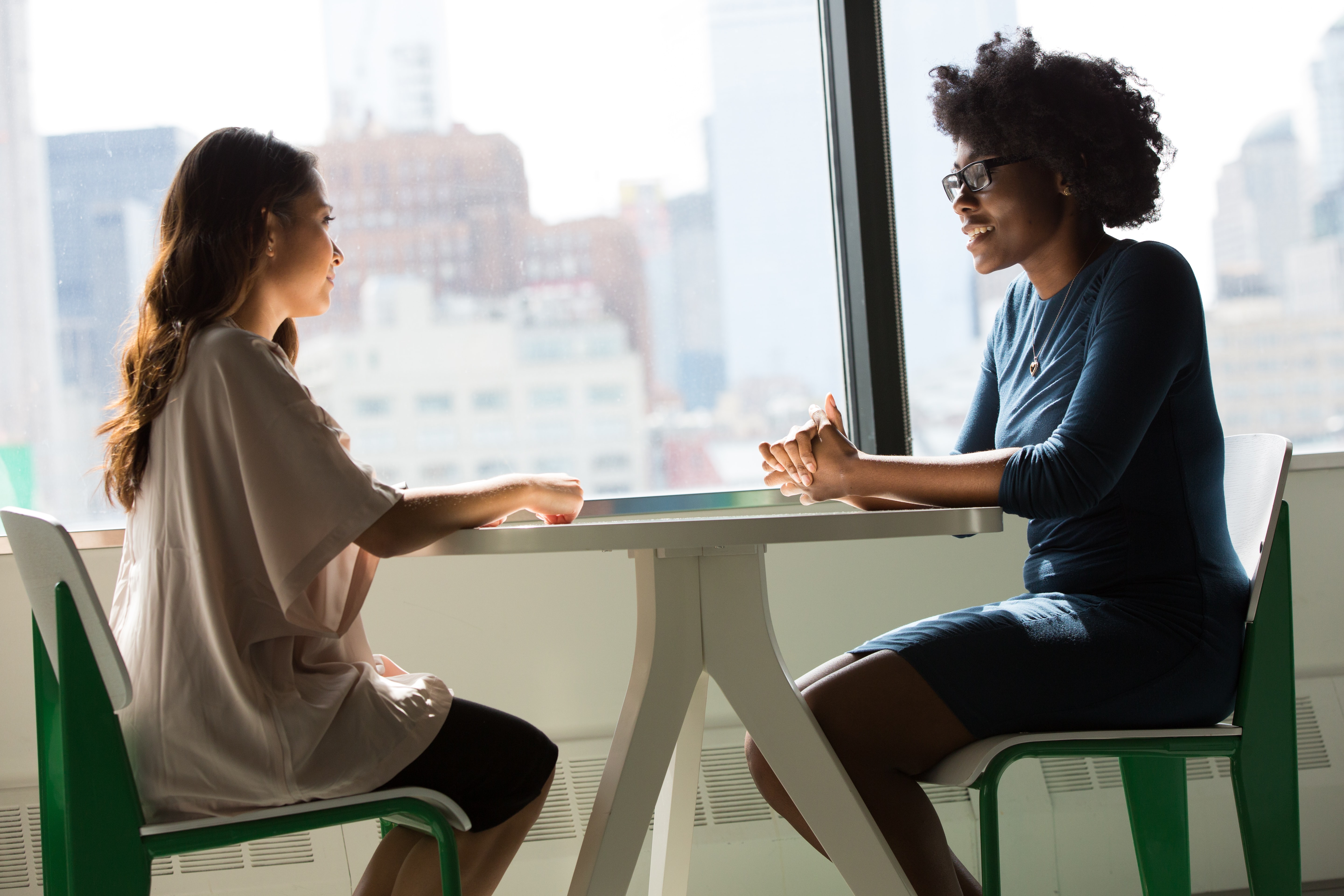 Two women sit across from one another at a small round table, talking.