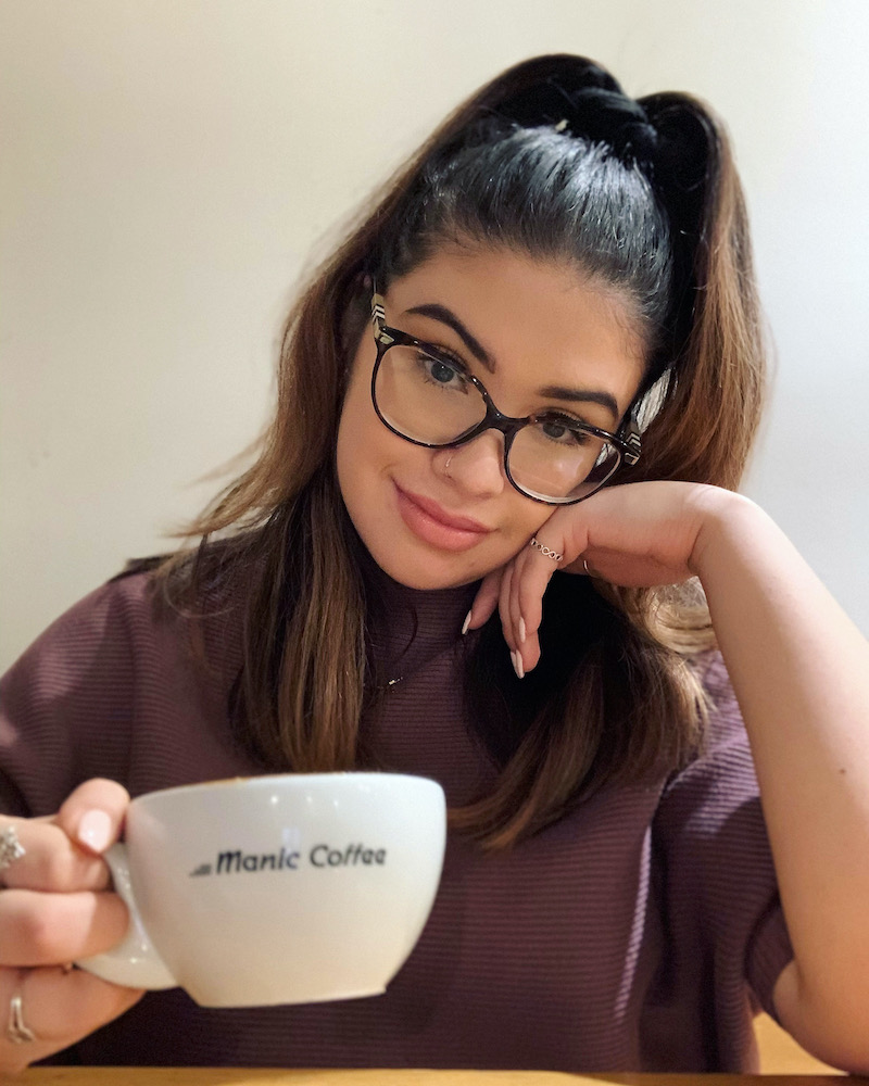 IGNITE Managing Editor, Sulvey Polanco holding a cup of coffee that reads Manic Coffee
